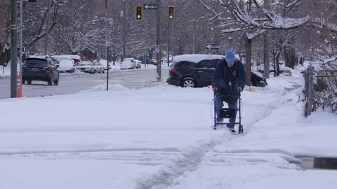 Elderly Man walks down snow covered streets with walker. Wide Stock Footage 86750711