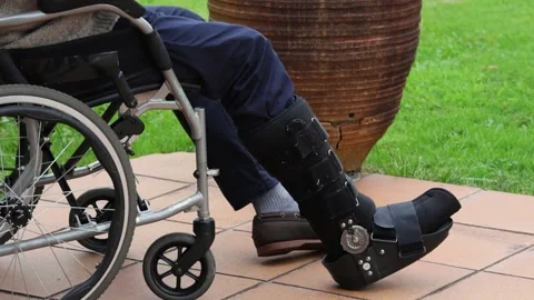 Elderly man wearing a walking boot resting his leg in a garden sitting in w.. Stock Footage 300172128