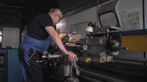 Elderly man in a work uniform works on a huge lathe Stock Footage 212401954