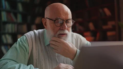 Elderly man working on laptop in library, feeling stuck with research progress 스톡 동영상 314056110