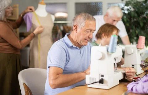 Elderly man working at machine during group practical sewing course Stock Photos