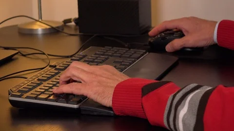 An elderly man works on a computer in an apartment - closeup on the keyboard 库存影片 115023965
