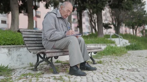 Elderly man writing on a notebook in a park Stock Footage 310597437