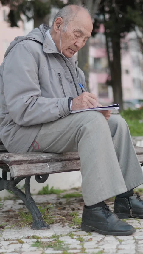 Elderly man writing on a notebook in a park Stock Footage 327229912