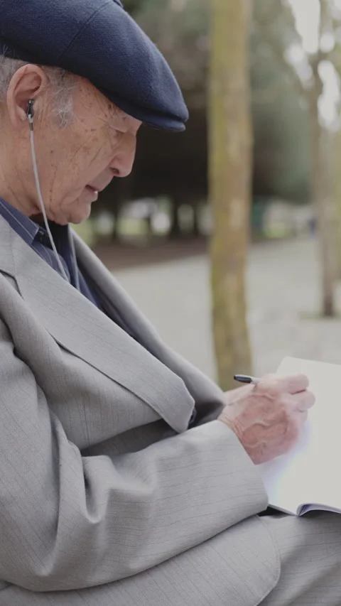 Elderly man writing in notebook while sitting on park bench Stock Footage 326821091