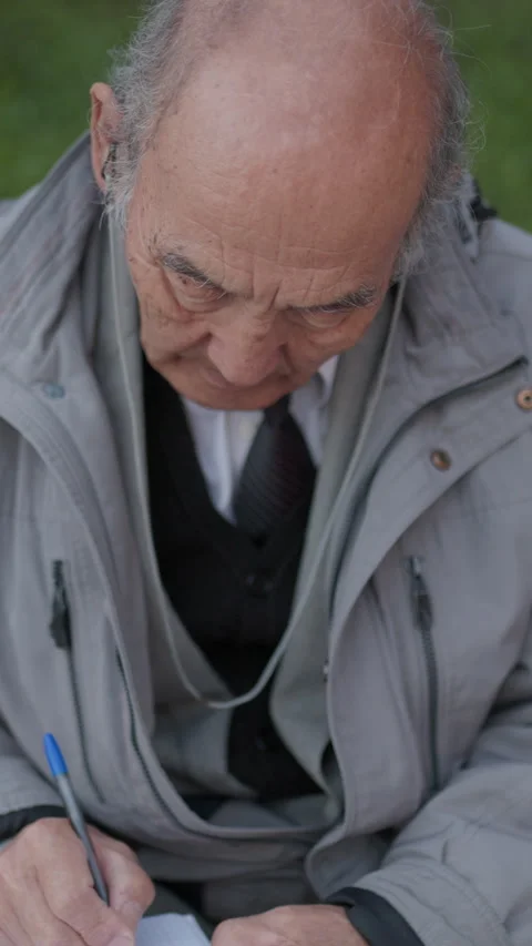 Elderly man writing on a notepad in a park Stock Footage 327230216