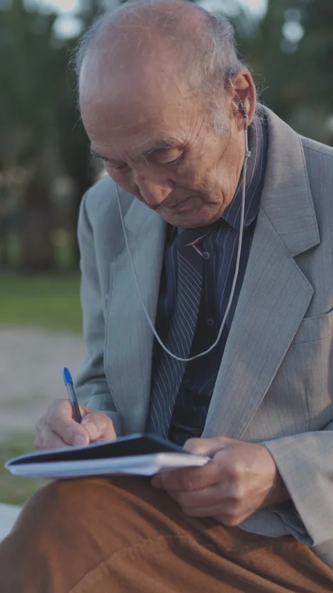 Elderly man writing on notepad in park Stock Footage 327235747