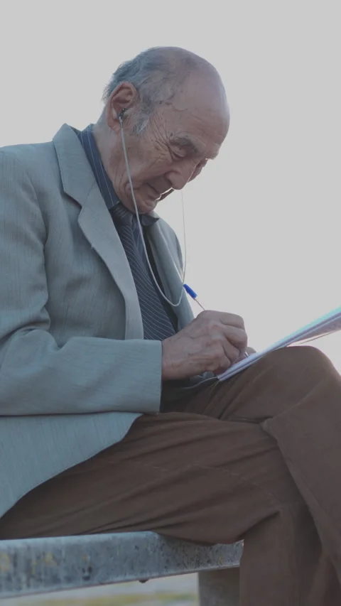 Elderly man writing on notepad in public park Stock Footage 327235787