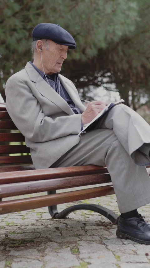 Elderly man writing on notepad while sitting on bench in park Stock Footage 326820915
