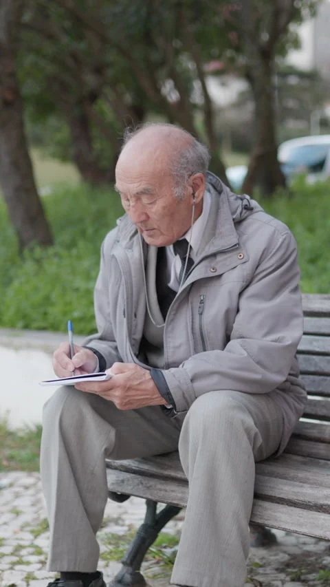 Elderly man writing on notepad while sitting on bench in park Stock Footage 327229862