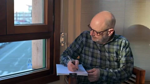 Elderly Man Writing At A Window Desk, Reflective Moment In A Quiet Home Study Stock Footage 329906324