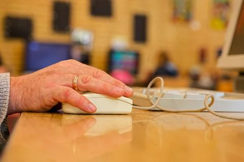 Elderly man's hand using a wired computer mouse on a wooden desk Stock Photos