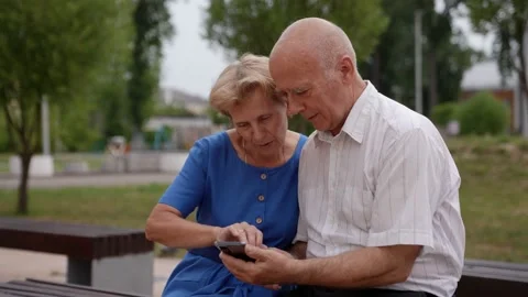 An elderly married couple enjoys using a mobile application in the park, holding Stock Footage 157448747
