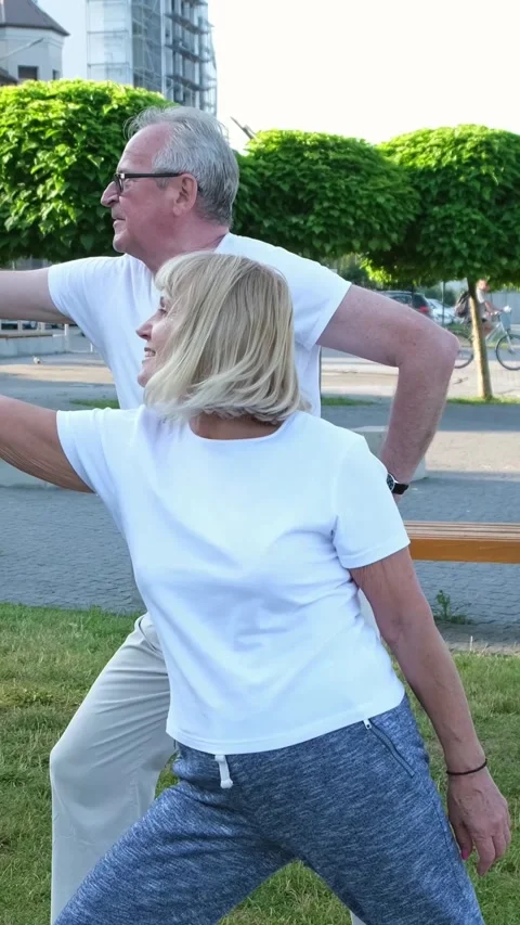 Elderly married couple is exercising doing yoga outdoors on the green lawn of Stock Footage 250383938