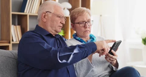 Elderly pair using mobile phone at home with digital guidance and tech support Stock Footage 331706122