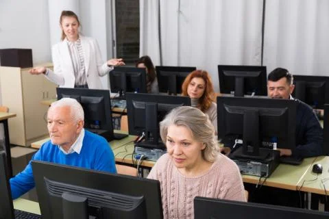 Elderly people working on computers with young teacher 스톡 사진