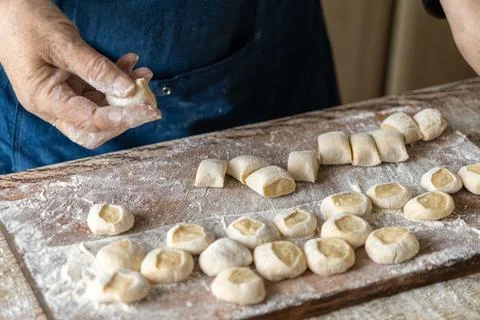 An elderly person forms small raw dumplings on a wooden board covered with .. Stock Photos