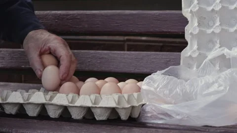 An elderly person placing brown eggs into a cardboard carton on a wooden be.. Vidéo 339850934