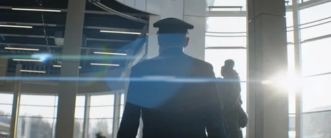 Elderly pilot in cap walks through airport terminal, illuminated by sunlight Stock Footage 123259483