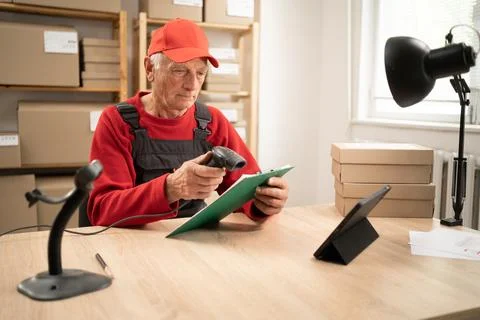 Elderly postal worker scanning barcode on parcel with handheld scanner at w.. Stock Photos
