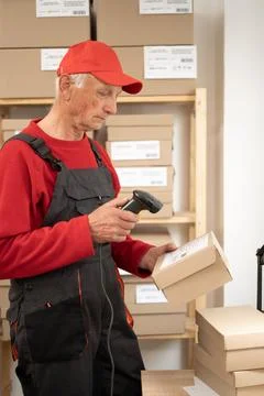 Elderly postal worker scanning barcode on parcel in logistics warehouse Stock Photos