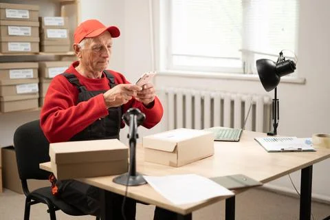 Elderly postal worker scanning barcode label at warehouse Stock Photos