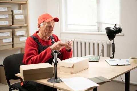 Elderly postal worker scanning parcel barcode at warehouse Stock Photos
