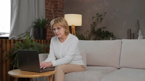 An elderly, pretty female programmer works at home on a laptop Stock Footage 233584285