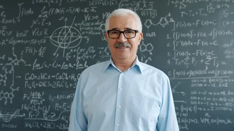Elderly professor smiling looking at camera standing near blackboard with Stock Footage 124868175