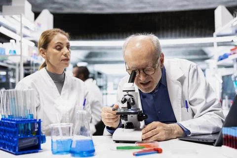 Elderly researcher and intern documenting cellular structures with microscope Stock Photos