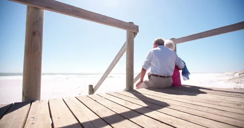 Elderly retired couple sitting together affectionately at the beach Stock Footage