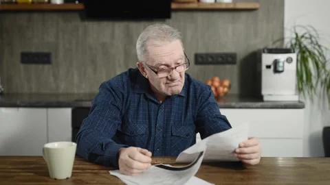 An elderly retired man sits at a table and deals with bills and documents. A man Stock Footage 234865903
