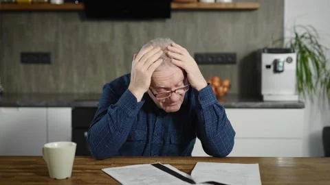 An elderly retired man sits at a table and deals with bills and documents. A man Stock Footage 234869018