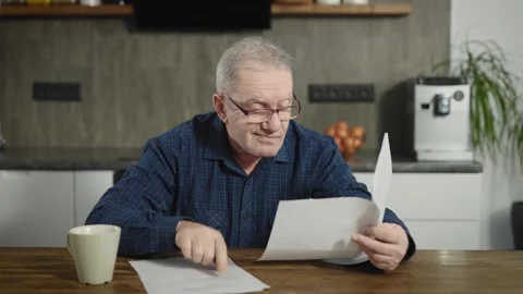 An elderly retired man sits at a table and deals with bills and documents. A man Stock Footage 236401009
