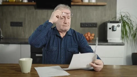 An elderly retired man sits at a table and deals with bills and documents. A man Stock Footage 236468365