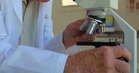 Elderly scientist examines a sample through a microscope. Vidéo 88371982