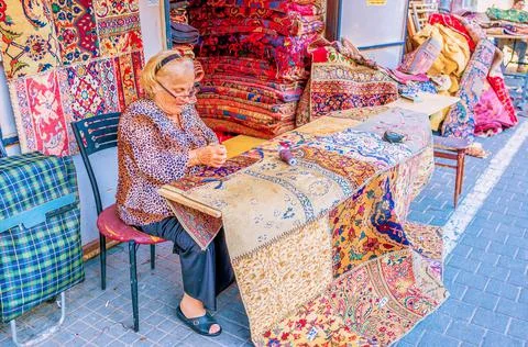 The elderly seamstress makes patchwork rugs on flea market in Tel Aviv, Israe Stock Photos