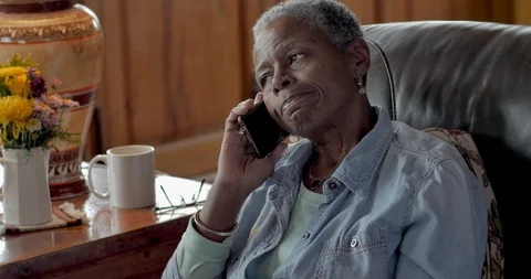 Elderly senior black woman talking on smart phone in her living room Stock Footage
