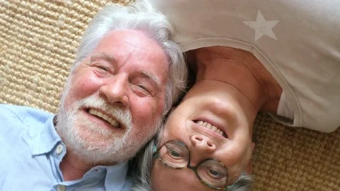 Elderly senior couple smiling while lying on carpet in living room at home, coup Stock Footage 166244482
