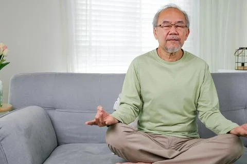 Elderly setting on sofa and doing yoga exercise Foto stock