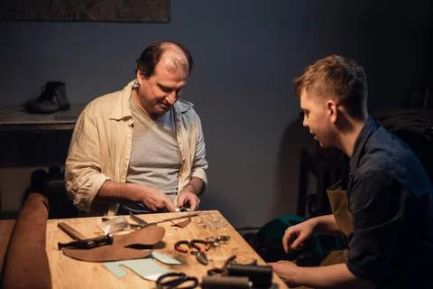 An elderly shoemaker and his apprentice create shoes by hand in their workshop Stock Photos