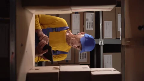 Elderly small warehouse employee checking inventory using digital tablet. Old Stock Footage 249597991