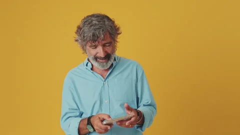 Elderly smiling grey-haired man playing video games on mobile phone, isolated on Stock Footage 255505345