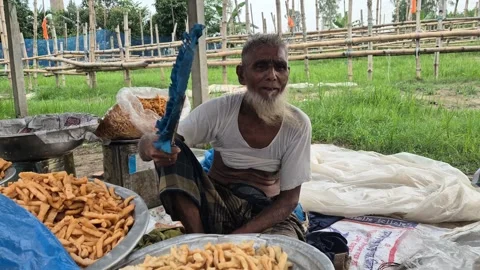 Elderly Street Vendor Using Hand Fan In Hot Weather In Bangladesh Vidéo 338437419