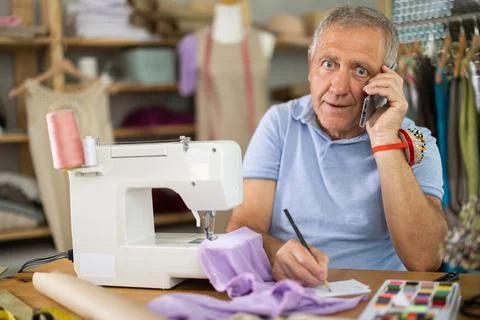 Elderly tailor taking notes while talking on phone Stockfoto's