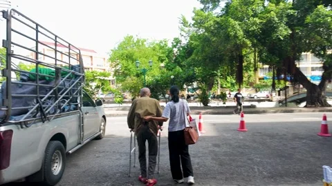 Elderly Thai Man Using Walker Assisted by Caregiver on Bangkok Street Stock Footage 339405275