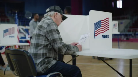 Elderly voter sits at voting booth and reads bulletin 動画素材 273864165