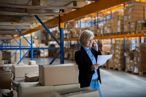 Elderly warehouse manager or supervisor reading document in clipboard. Stock Photos