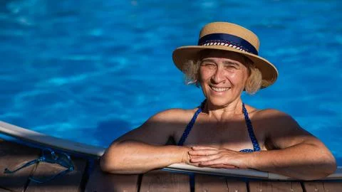 An elderly woman in a boater hat swims in the pool. Vacation in retirement. Stock Photos