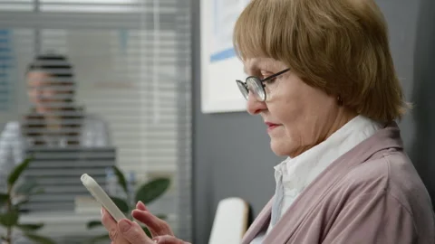 Elderly Woman Browsing Phone while Waiting Appointment at Doctors Office Stock Footage 333202800